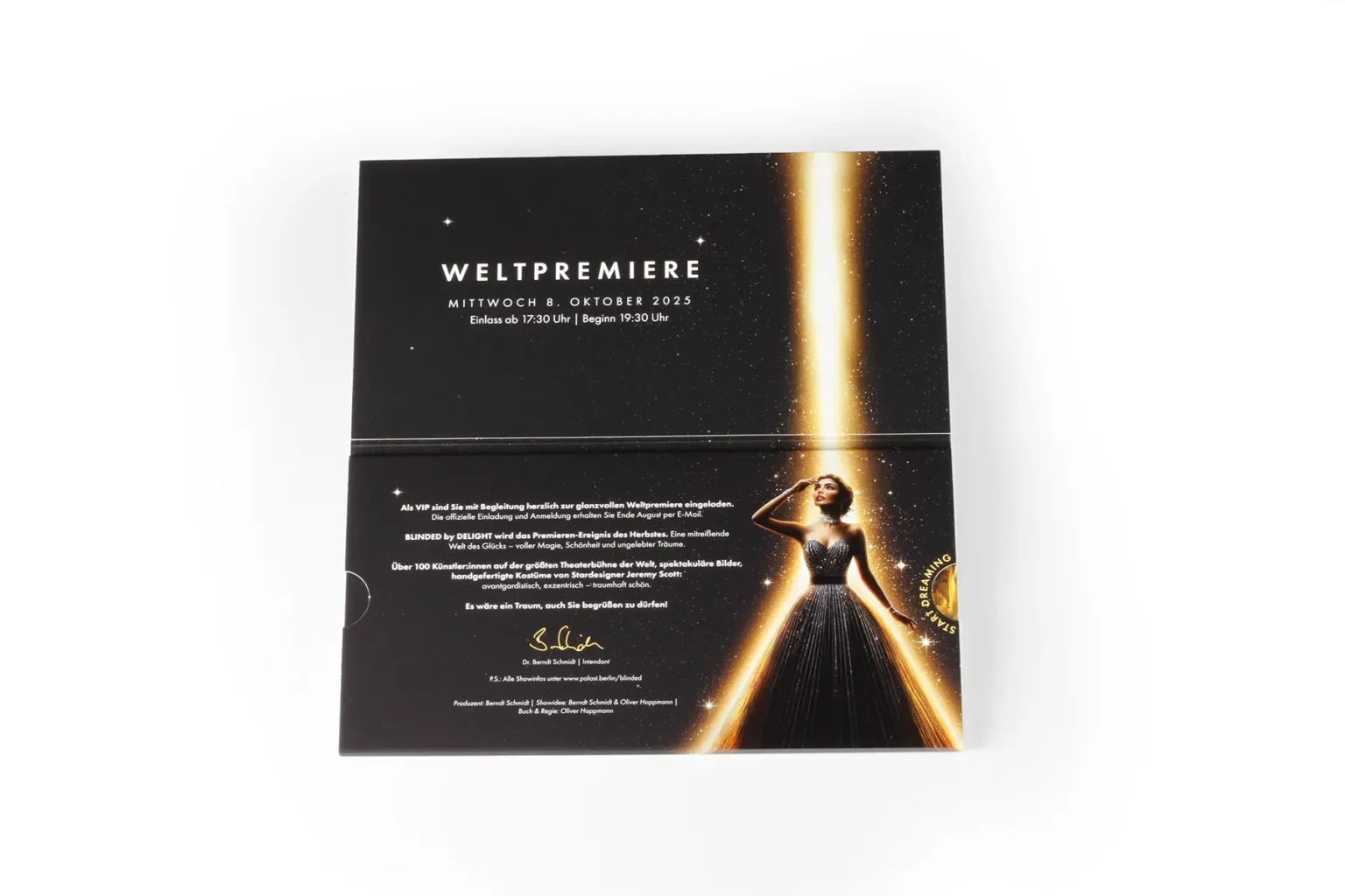 Aufgeklappte Schiebeschachtel zeigt Weltpremiere-Ankündigung und Frau im Abendkleid im goldenen Lichtstrahl